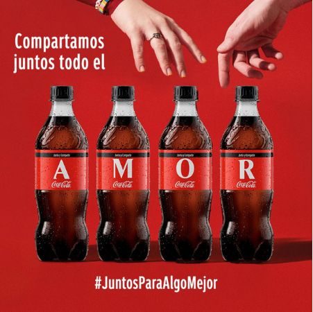 Creatividad de CocaCola para San Valentín en la que aparecen dos manos a punto de tocarse al intentar coger unas Coca-Colas.  En la imagen se lee "Compartamos todo el amor juntos"cada letra de la palabra amor está en la etiqueta de una coca cola