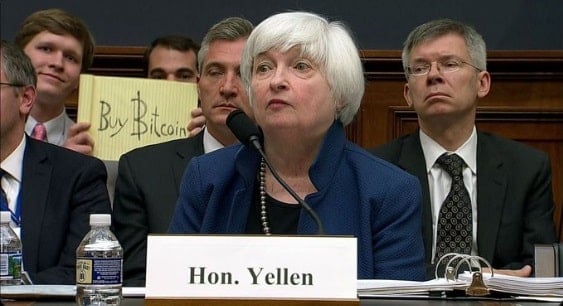 niño sosteniendo un cartel improvisado "comprar bitcoins" detrás de Janeth Yellen en el Congreso de los Estados Unidos