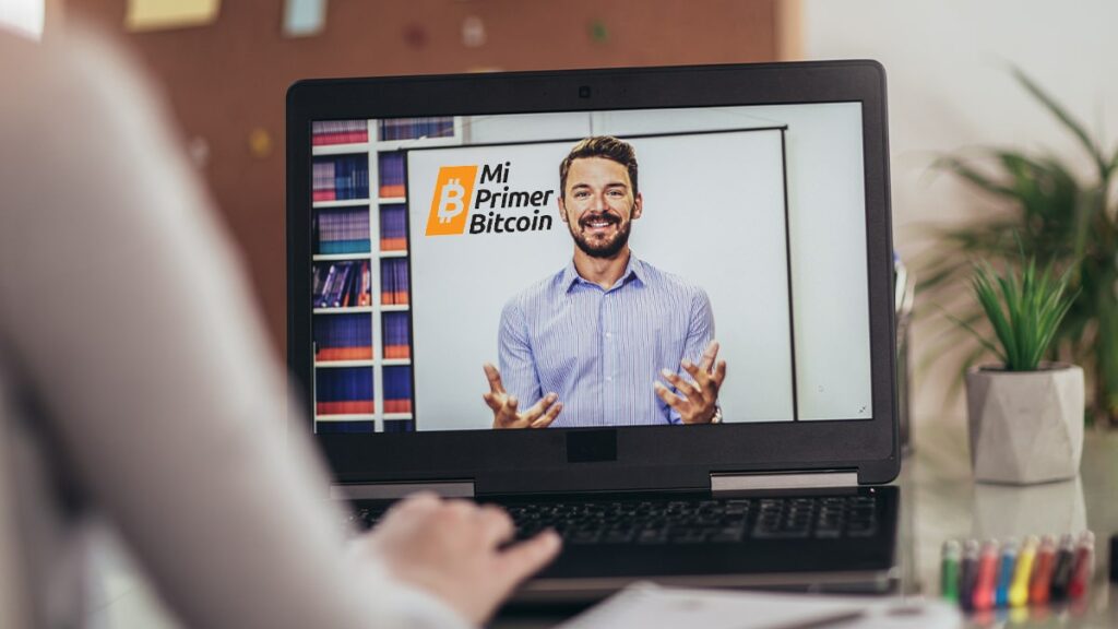 Persona viendo clases en línea en la pantalla de la computadora con el logo My First Bitcoin en la pizarra